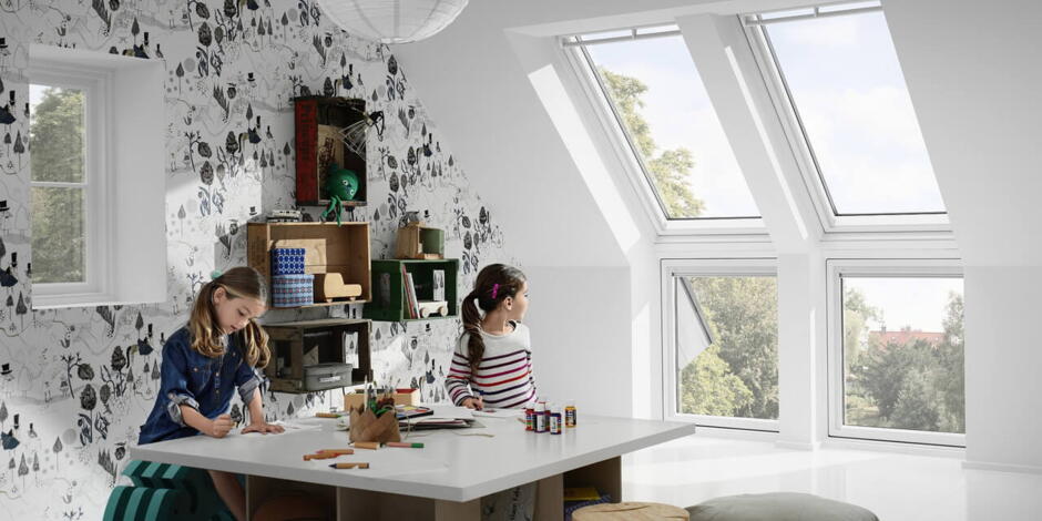 Kinder schauen beim Spielen und Lernen im hellen Kinderzimmer aus den großen Fenstern | VELUX Magazin